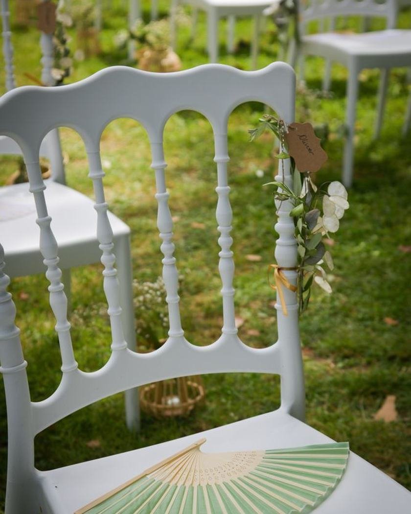 Éventail vert d’eau posé sur l’assise d’une chaise blanche, sur la pelouse